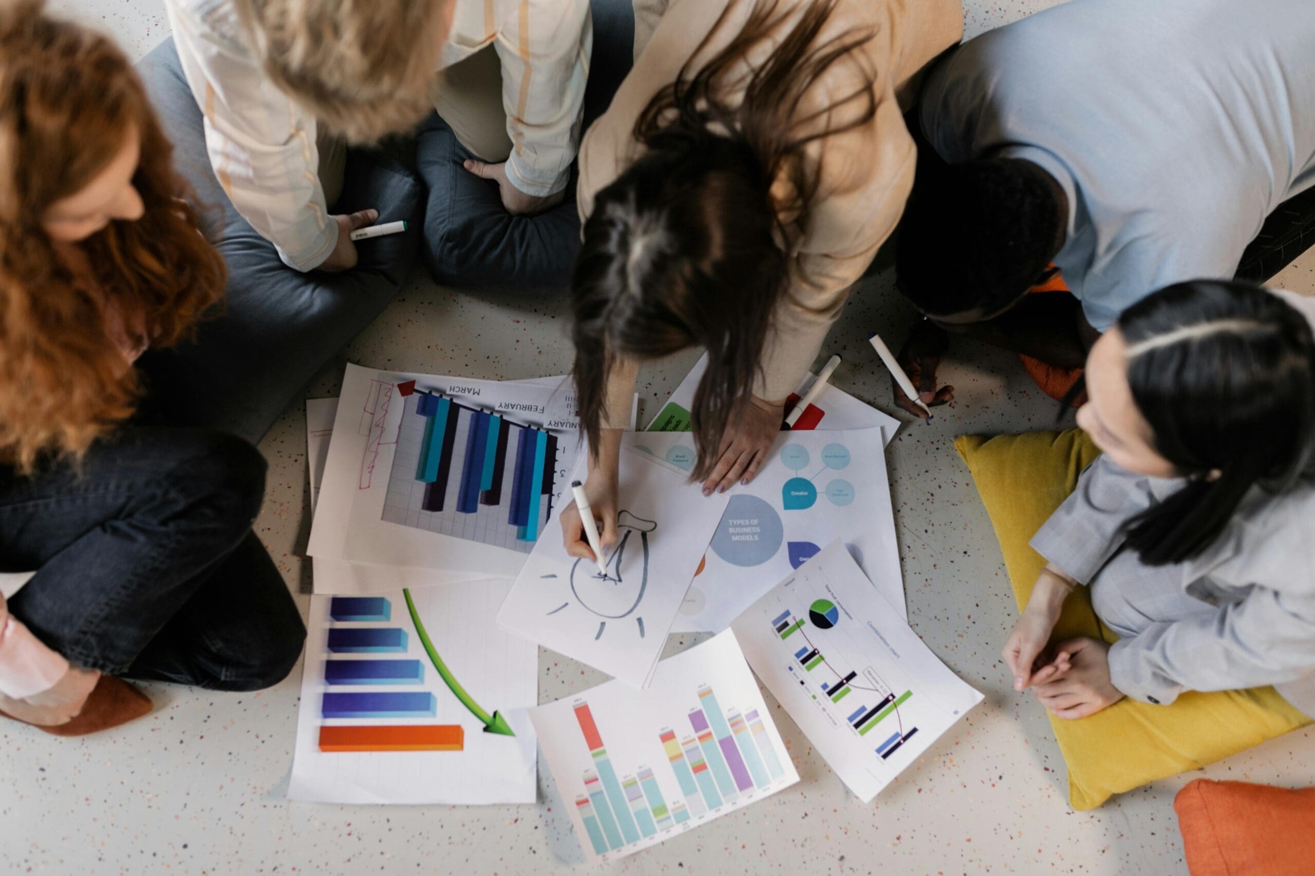 team in a circle on the floor, with papers that include charts and graphs