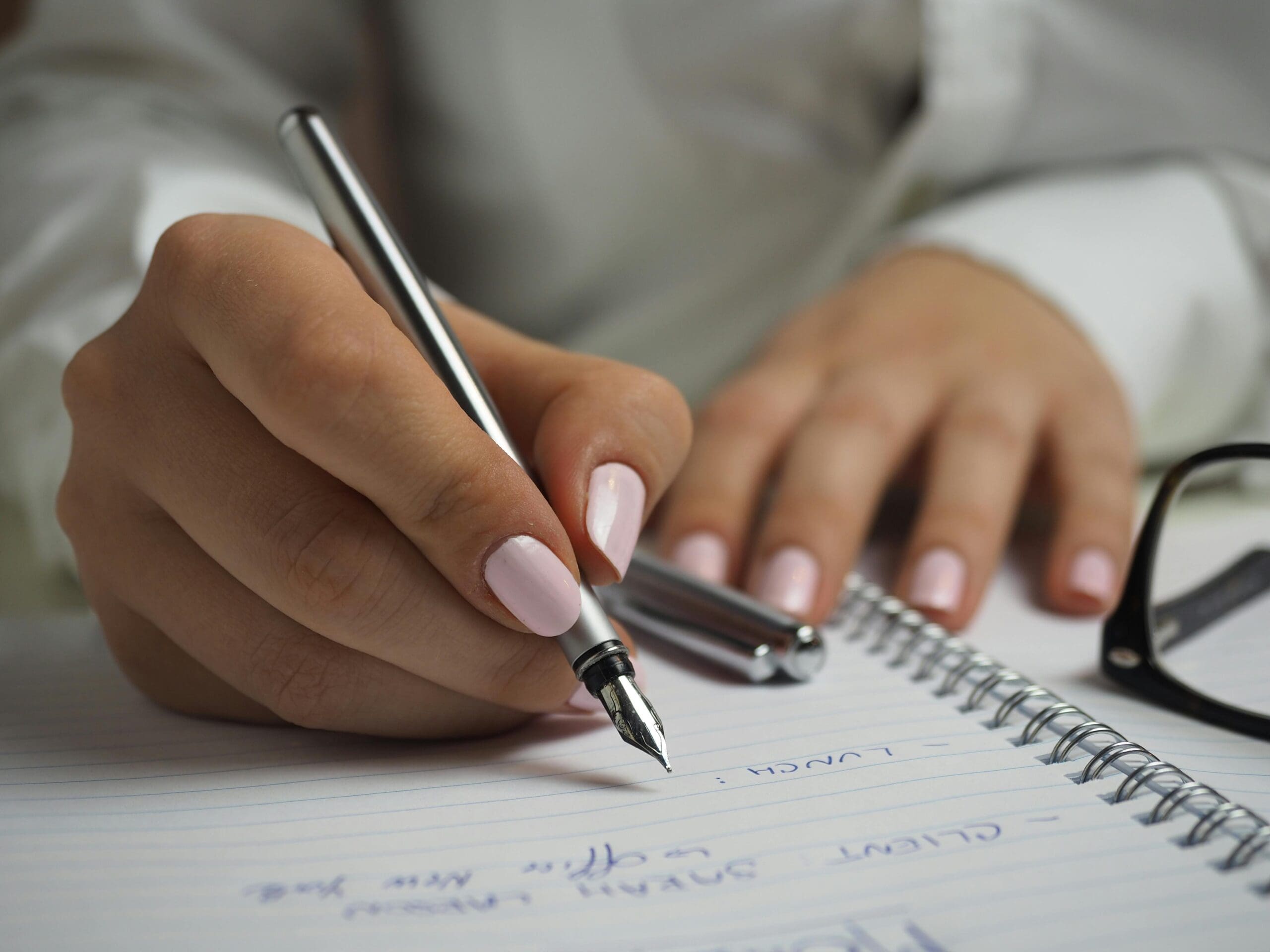hands with pink nail colors writing on a notepad