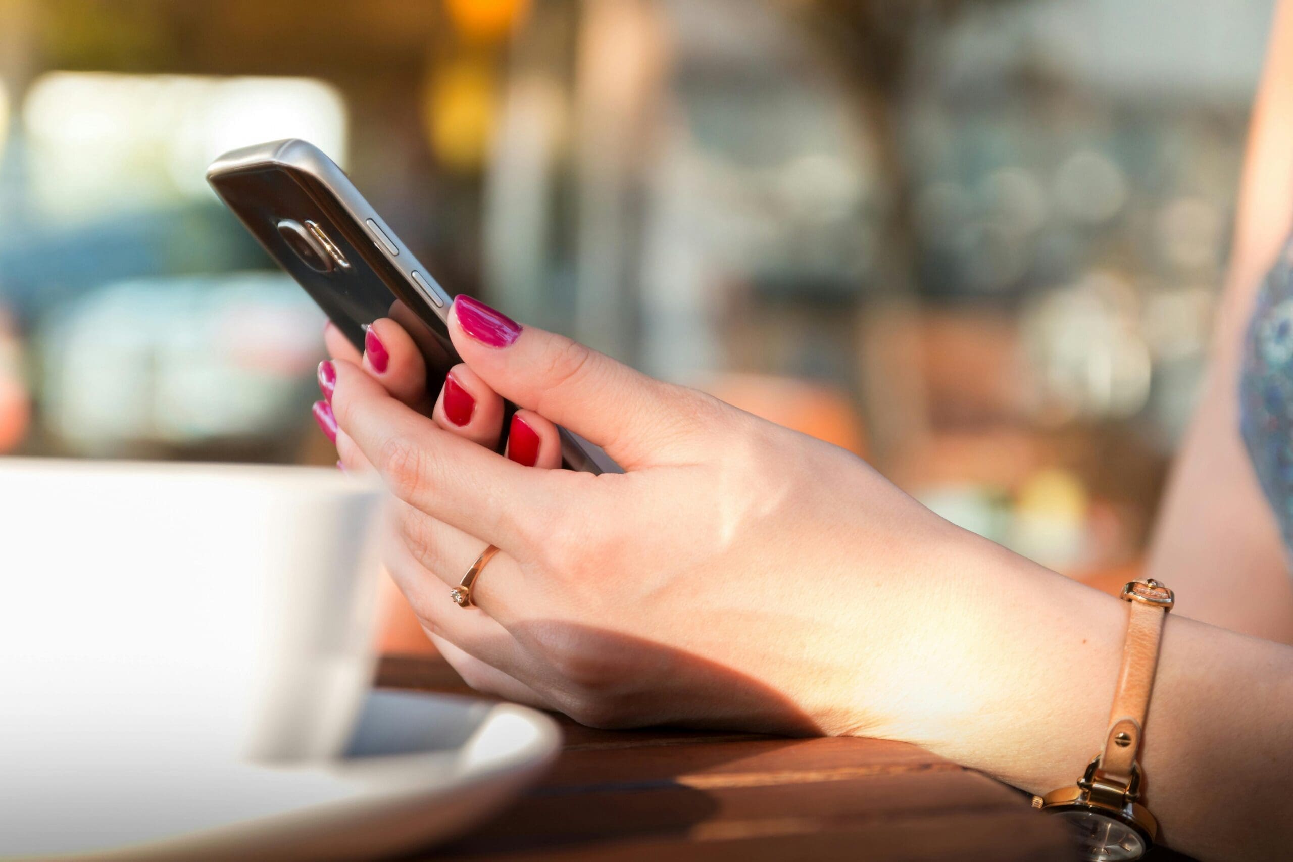 female hand holding phone next to coffee mug